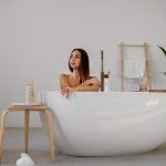 Cadă freestanding albă într-un decor minimalist de baie, cu accente naturale și atmosferă relaxantă